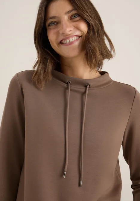 Lächelnde Frau mit braunem Kapuzenpulli.